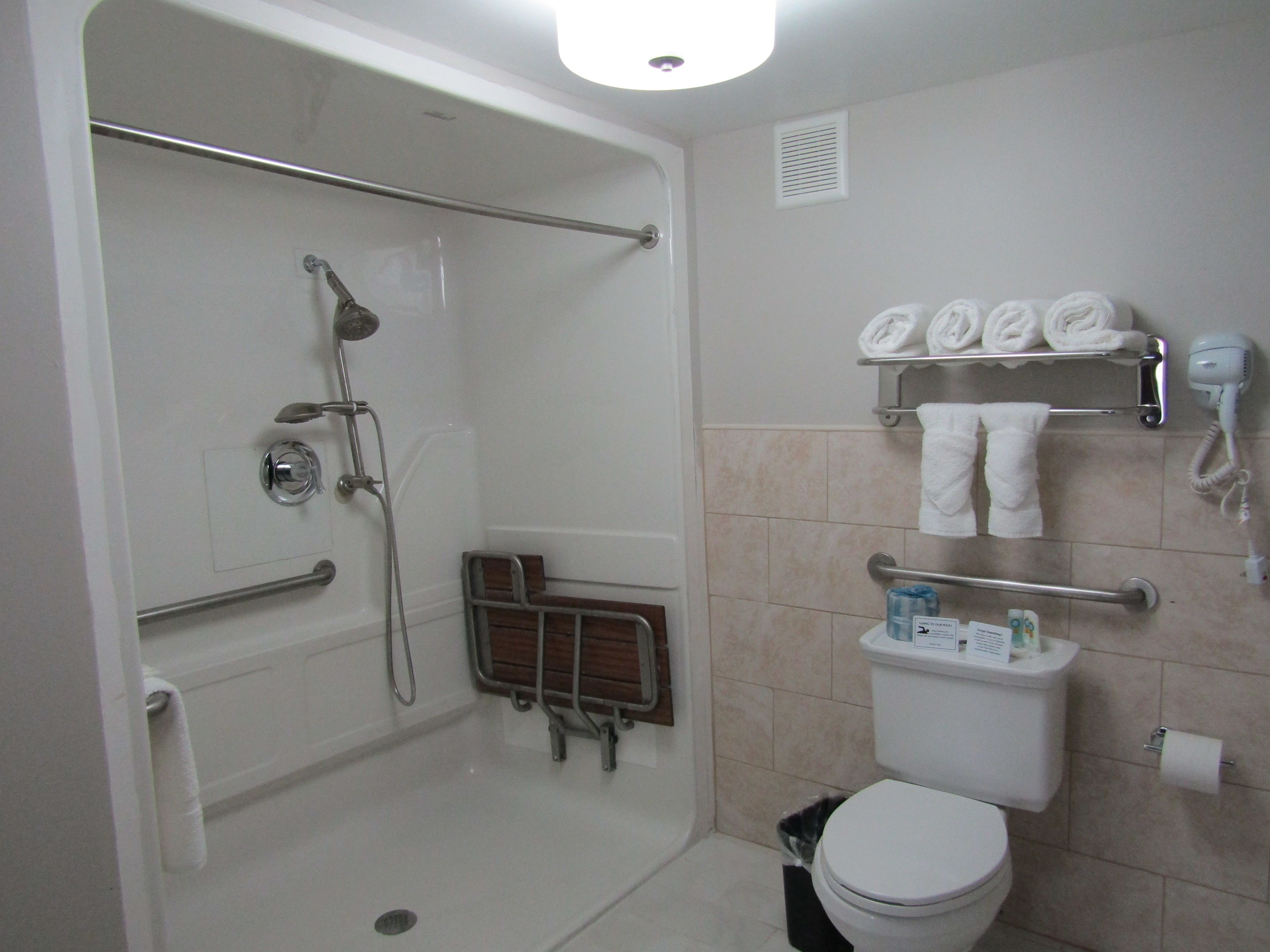 Un baño con cabina de ducha, inodoro, estante con toallas y secador de pelo.