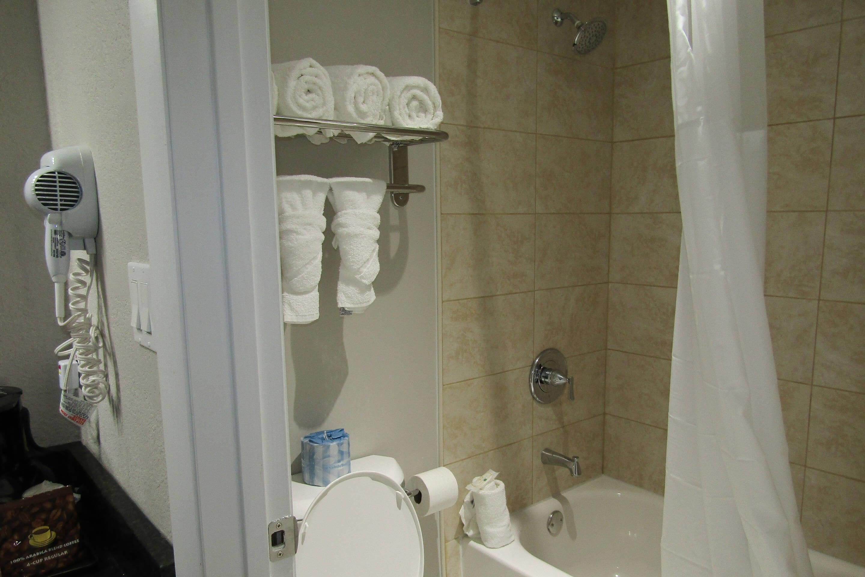Un baño con ducha, un secador de pelo y toallas en un perchero.