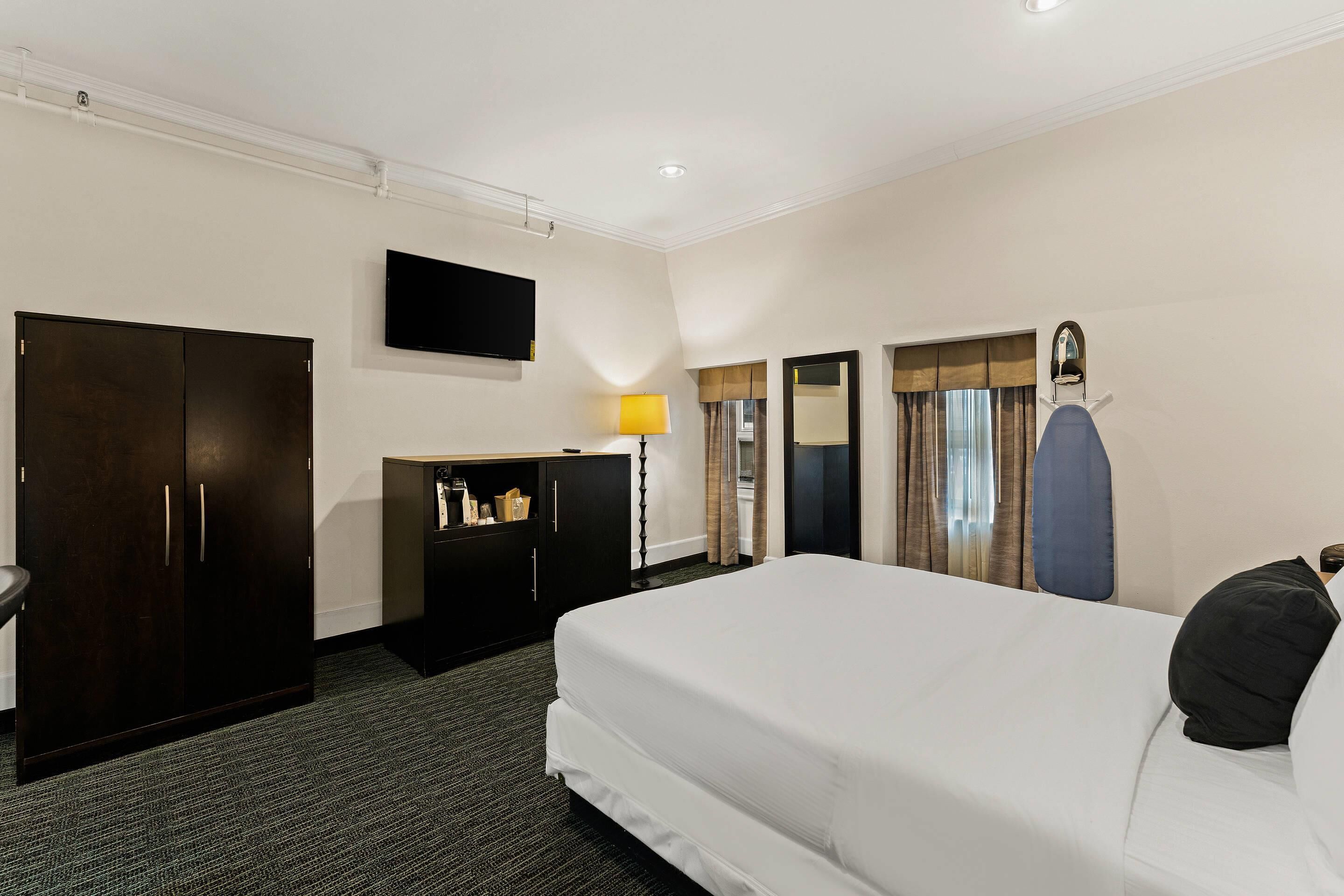 Une chambre d’hôtel avec un grand lit, une armoire, un bureau avec une lampe, une télévision et un miroir.