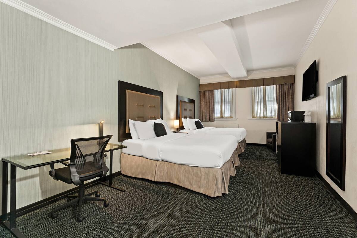 A hotel room with two beds, a desk, a chair, a TV, and a large mirror.