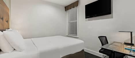 Habitación de hotel con una cama individual, un escritorio con silla, un televisor de pantalla plana en la pared y una ventana con persianas.