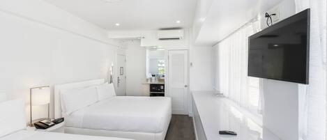 Et moderne hotelværelse med to senge, et fladskærms-tv, et natbord med lampe og udsigt til en gang med en dør.
