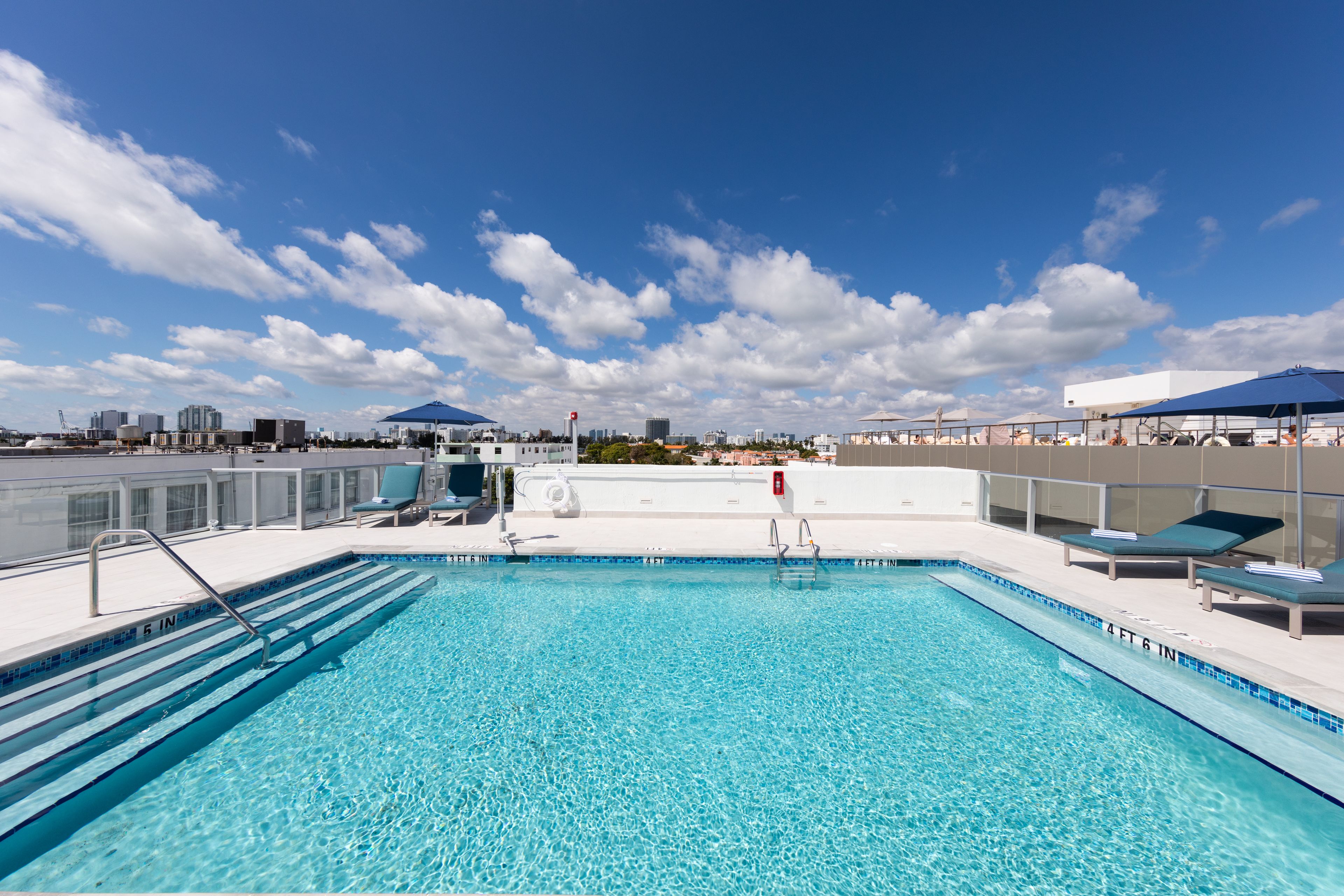 A rooftop swimming pool with clear blue water, lounge chairs, and umbrellas.