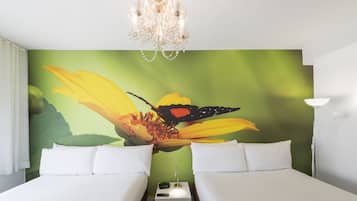 Une chambre d’hôtel avec deux lits, un lustre, une table de chevet avec une lampe et une fresque murale représentant une fleur et un papillon.