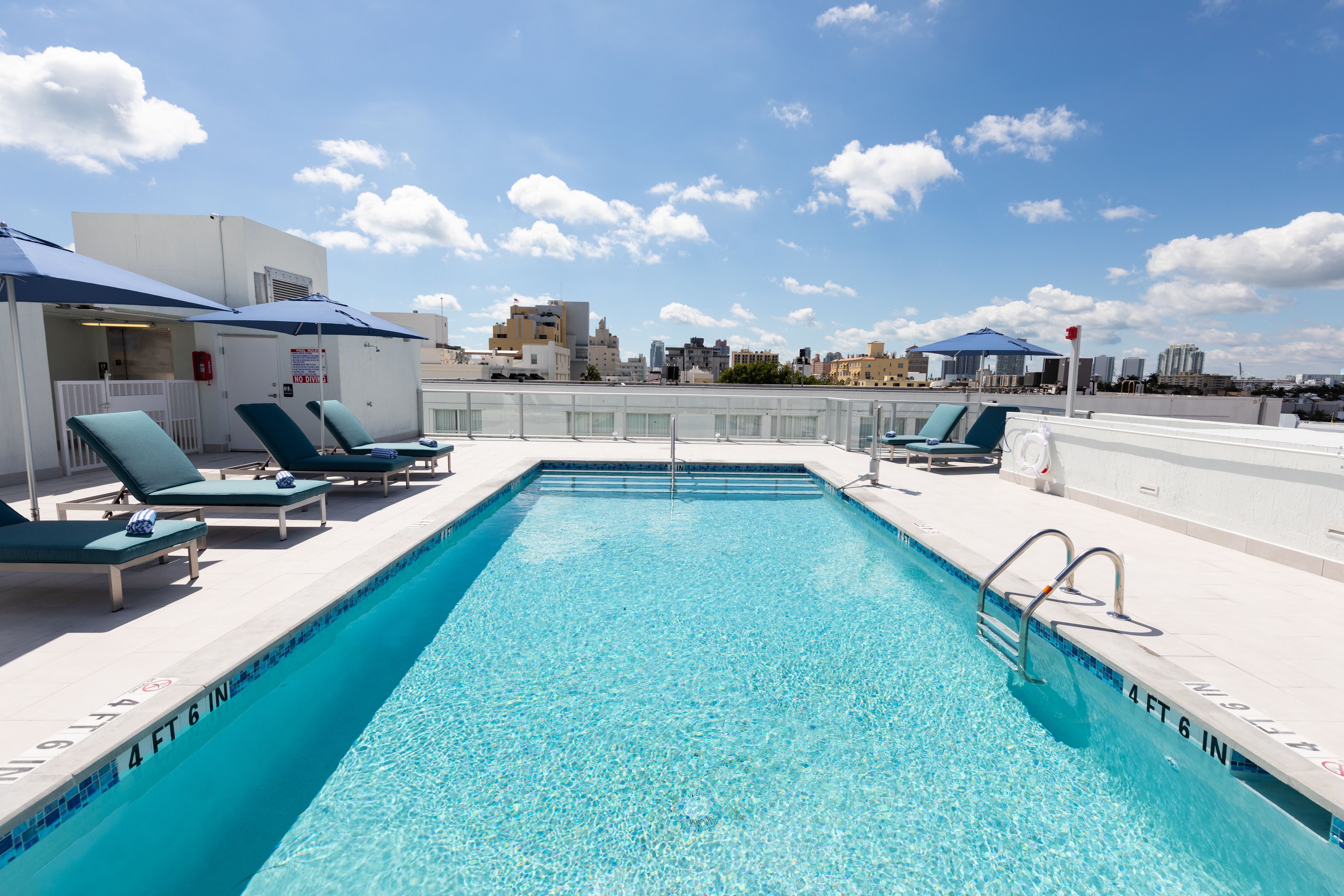 Une piscine sur le toit, avec une eau d’un bleu cristallin, entourée de chaises longues et de parasols, et en arrière-plan, une vue sur la ville.