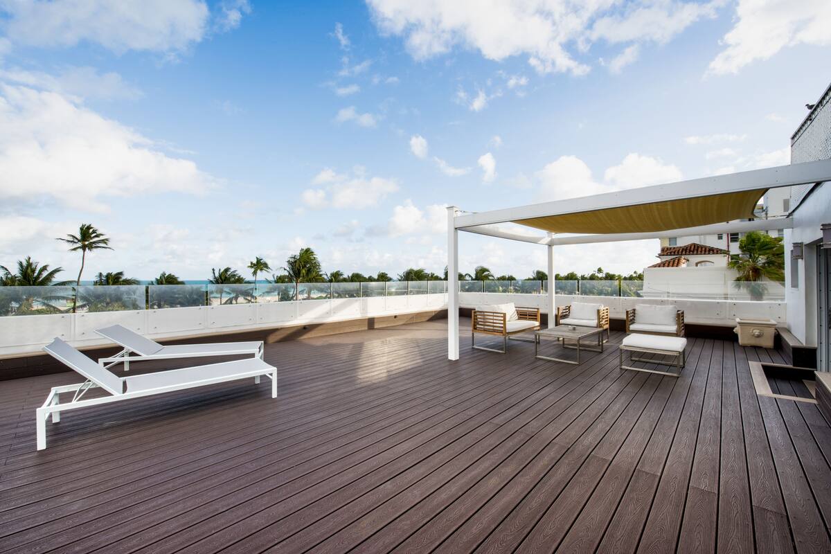 A wooden deck with lounge chairs and a covered seating area, overlooking a coastal landscape.