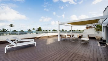 Eine Holzterrasse mit Liegestühlen und einem überdachten Sitzbereich mit Blick auf eine Küstenlandschaft.