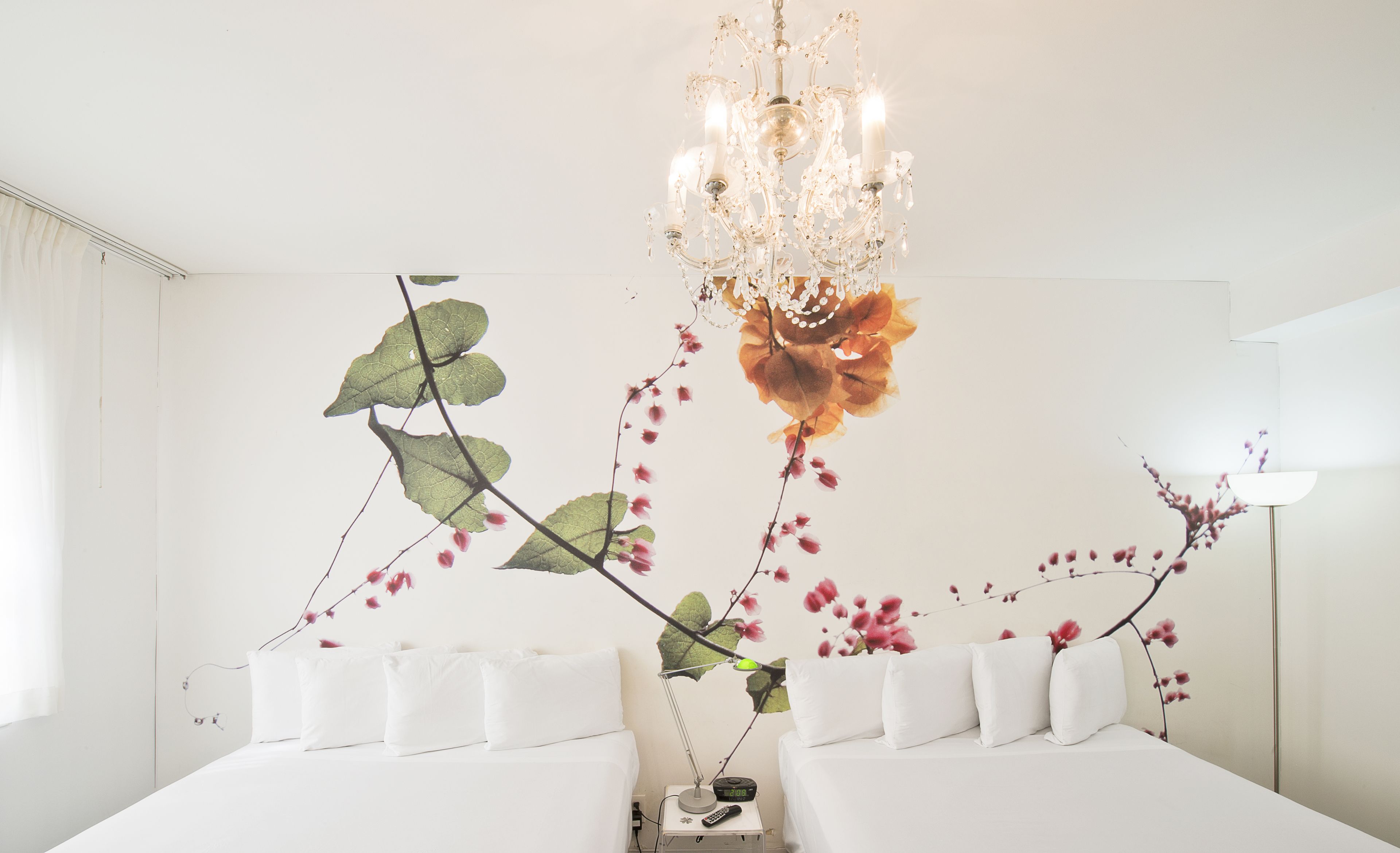 A hotel room with two beds, a chandelier, and a wall mural of a plant.