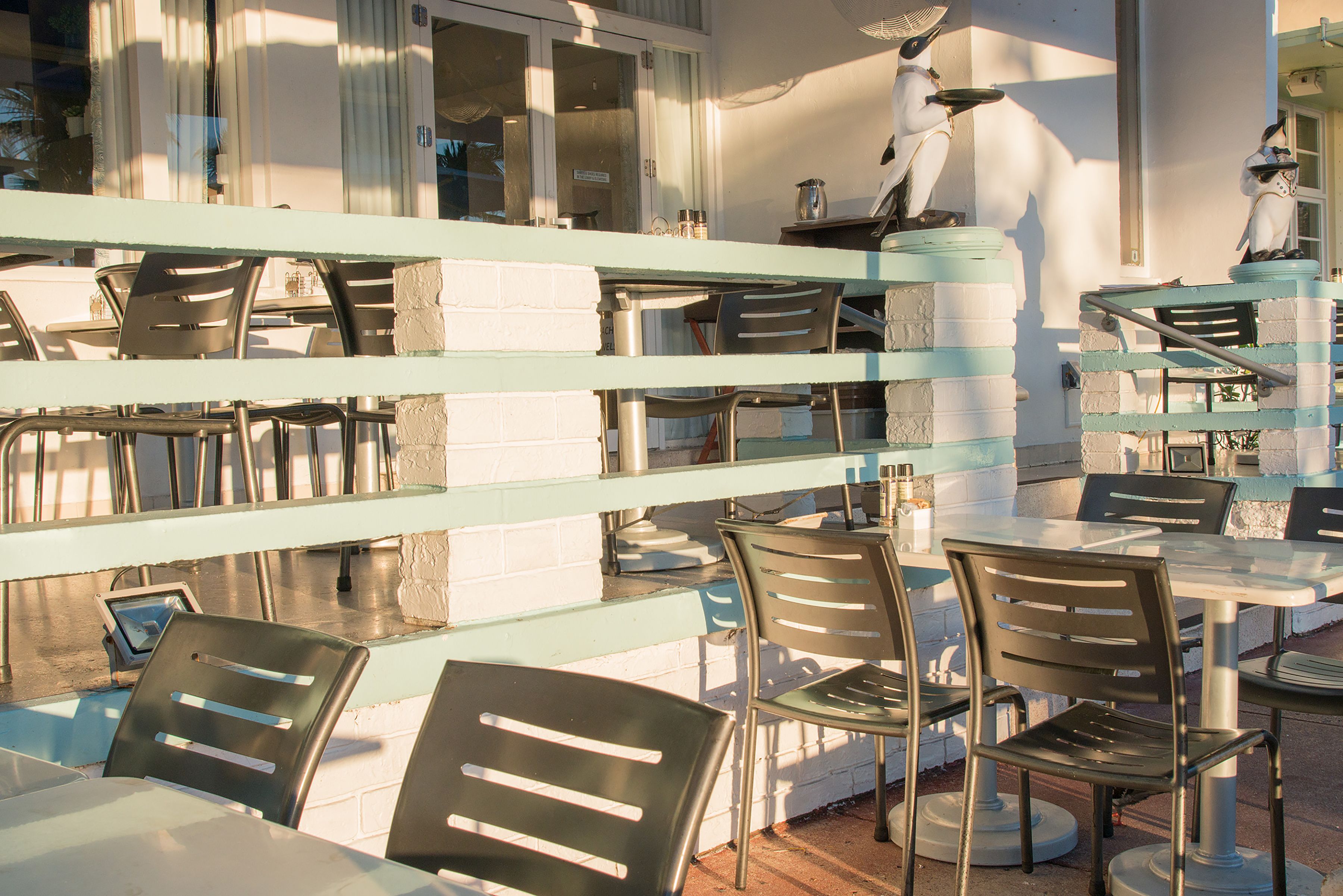 Un espace extérieur aménagé avec des tables et des chaises, un mur en briques et des statues d’oiseaux décoratives.