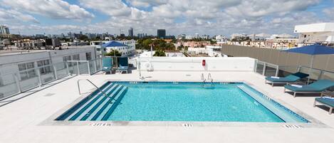 A rooftop pool with lounge chairs and a city view.