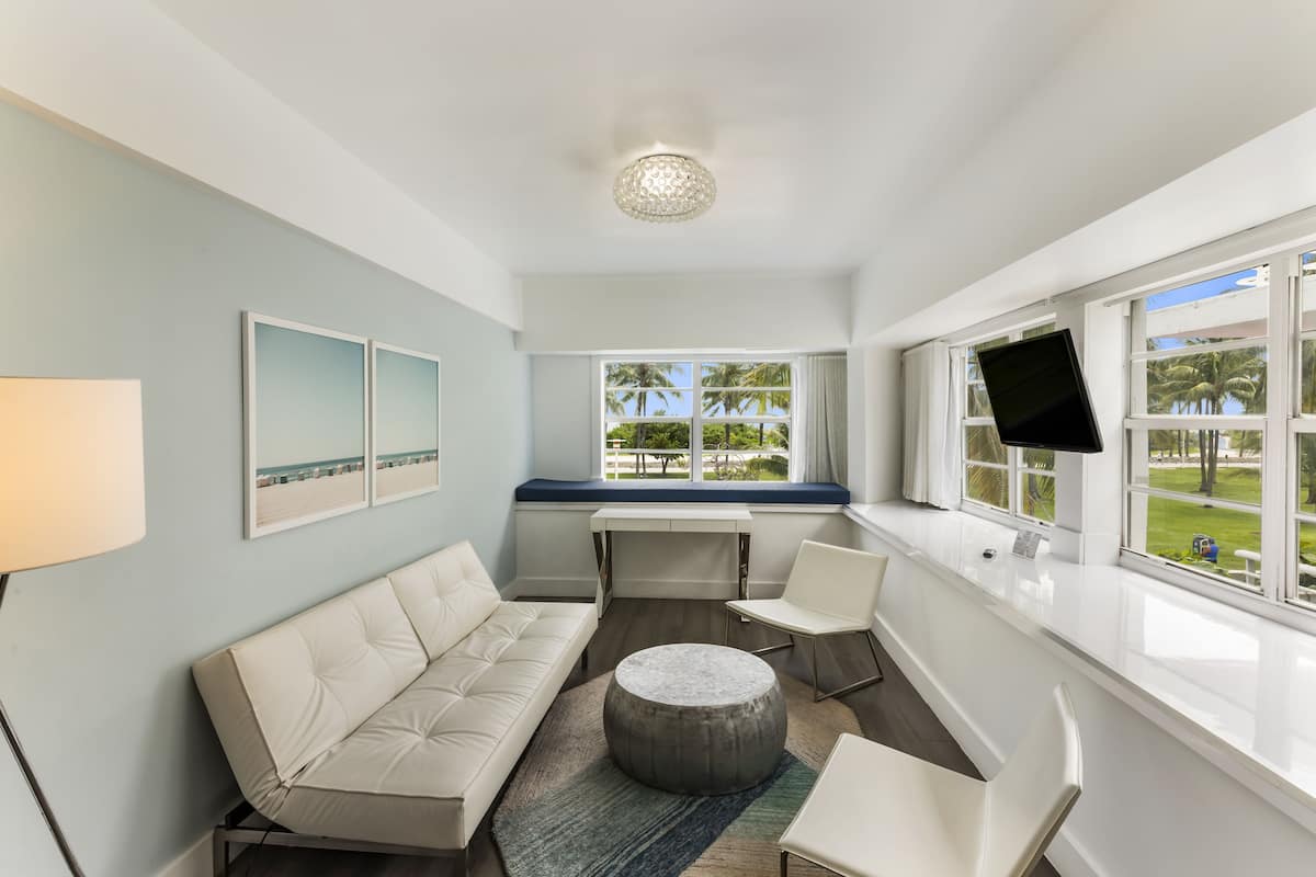 A modern living room with a sofa, chairs, a round ottoman, a desk, and a TV.