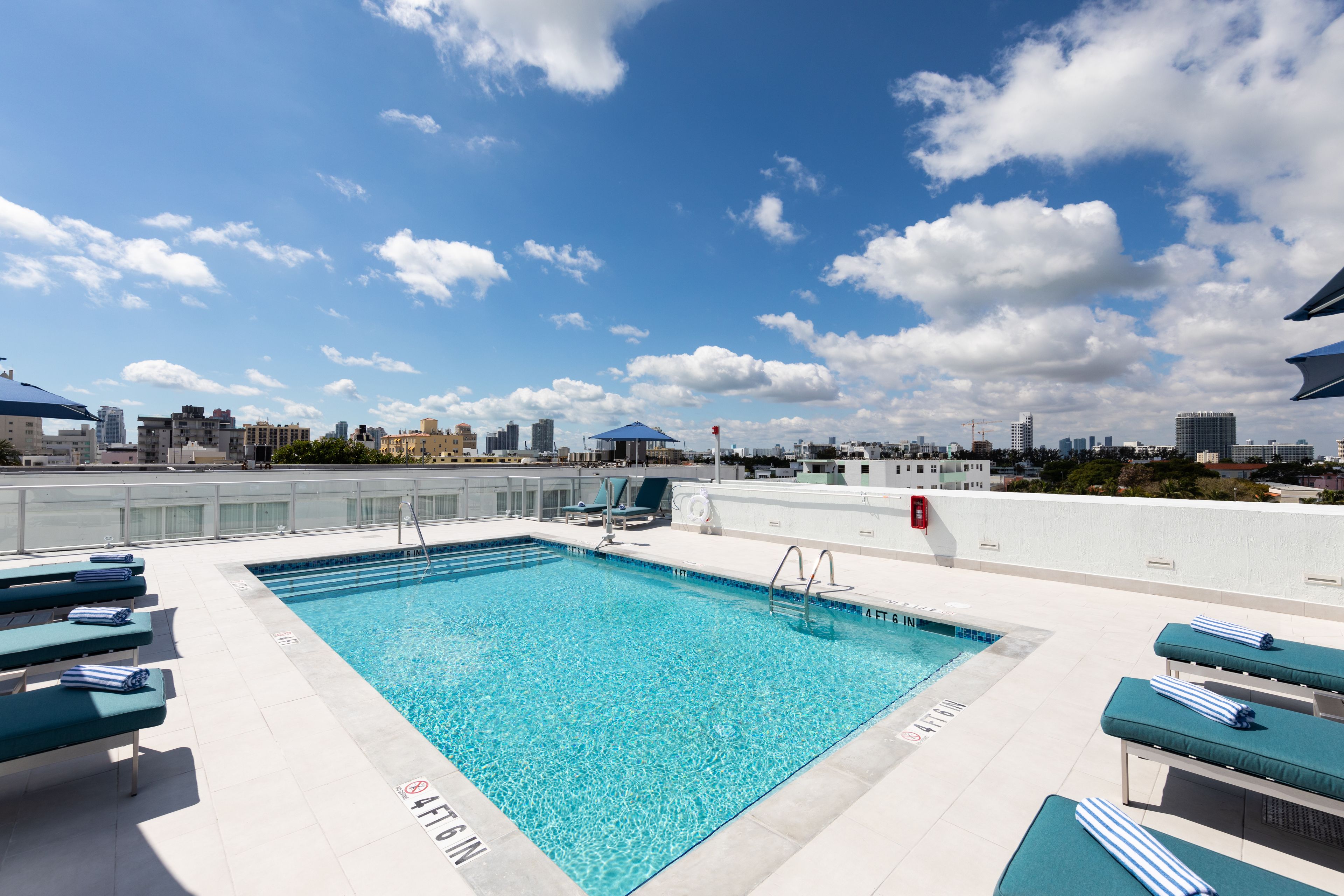 A rooftop pool with clear blue water, lounge chairs, and a city skyline in the background.