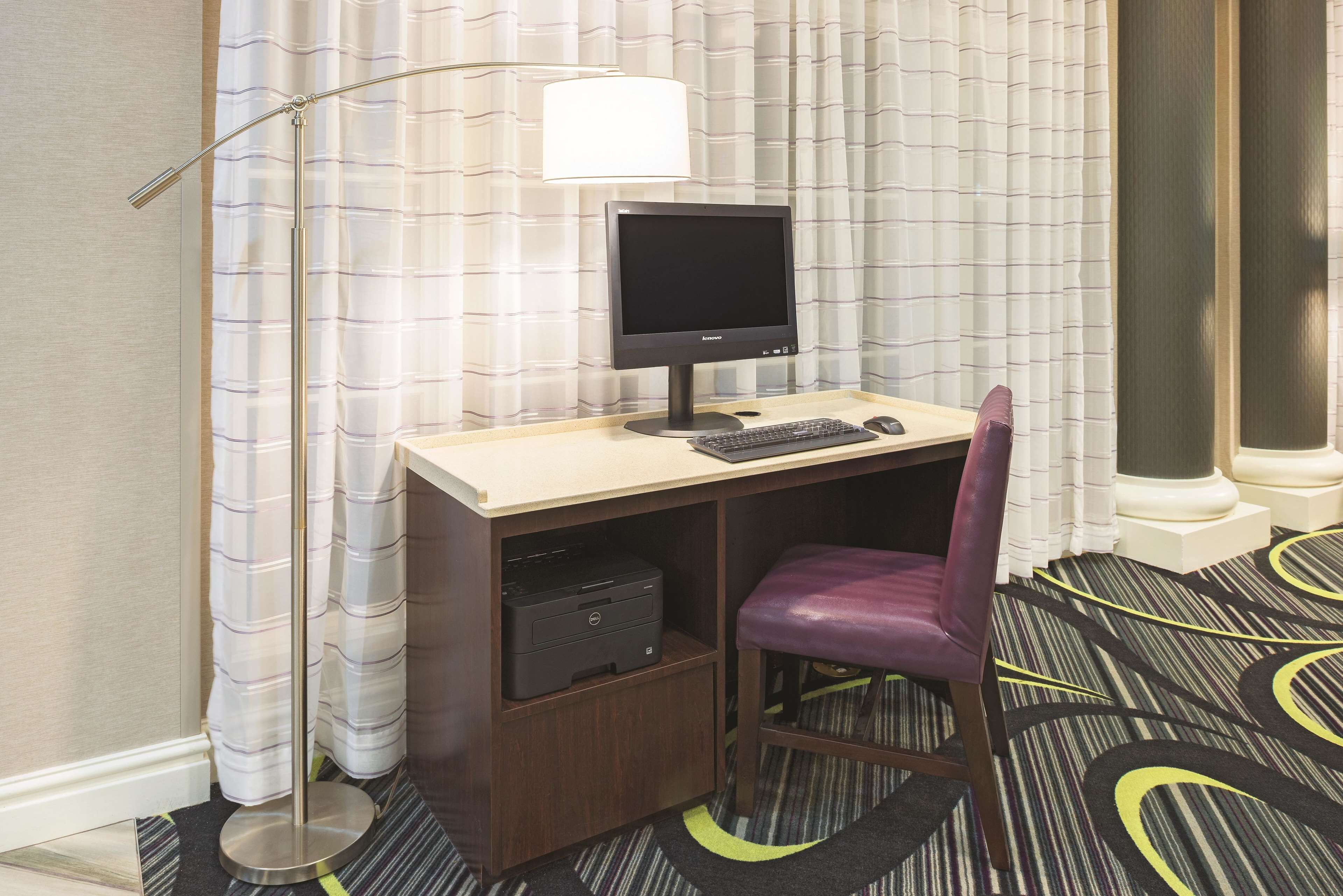 Quarto de hotel com escrivaninha, computador, impressora e uma cadeira roxa.