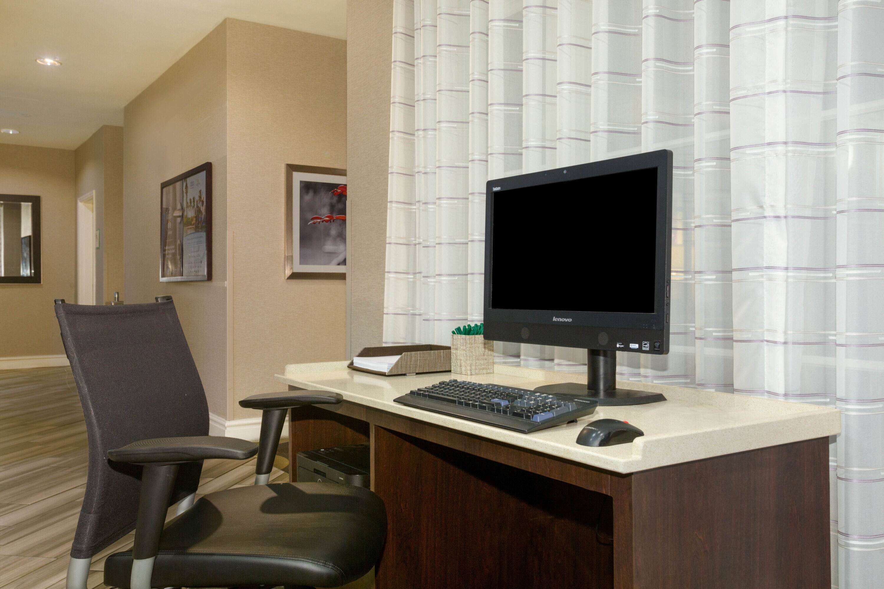 A hotel office with a desk, computer, keyboard, mouse, and a chair.