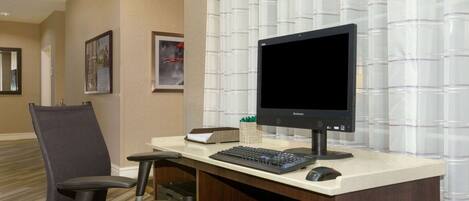 A hotel office with a desk, computer, keyboard, mouse, and a chair.