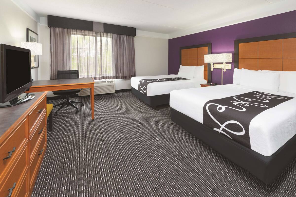 Une chambre d’hôtel avec deux lits, un bureau, une télévision et une fenêtre avec des rideaux.