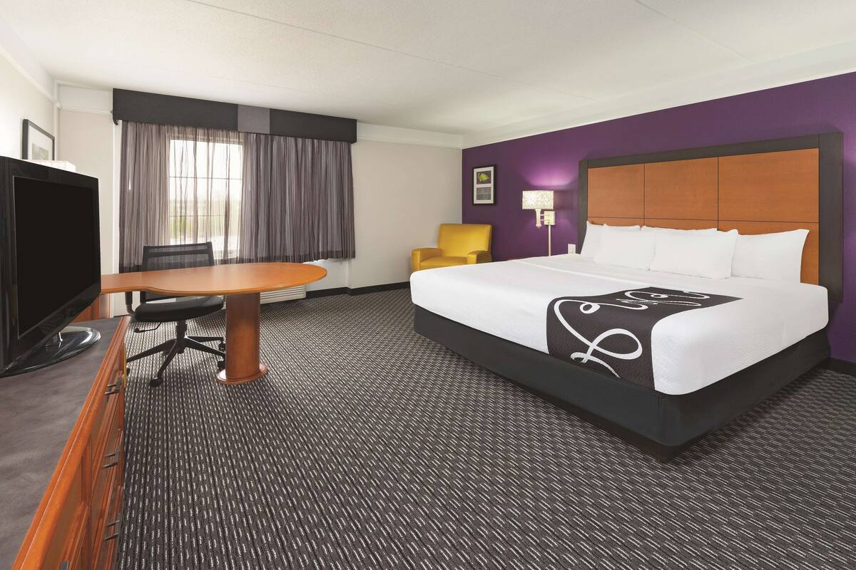 Une chambre d’hôtel équipée d’un lit, d’un bureau, d’une chaise, d’une télévision et d’une fenêtre avec des rideaux.
