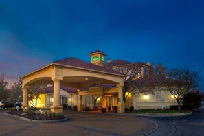 A hotel with a covered entrance, a tower with signage, and a landscaped area with planters. - La Quinta Inn & Suites by Wyndham St. Louis Westport (Maryland Heights)