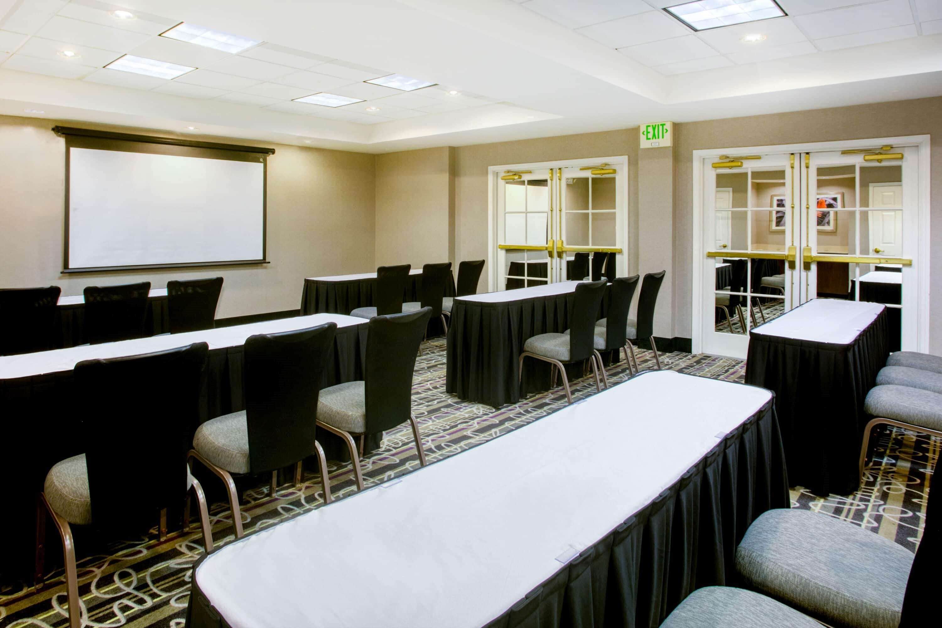 A conference room with a large table, chairs, a projector screen, and a carpeted floor.