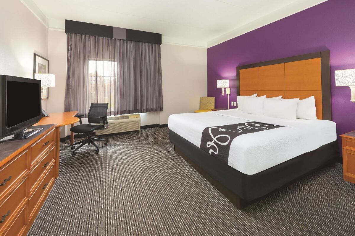 Une chambre d’hôtel avec un lit, un bureau, une télévision et une fenêtre avec des rideaux.