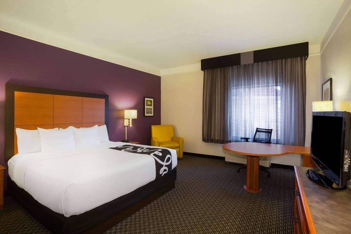 Une chambre d’hôtel avec un grand lit, un bureau, une chaise, une télévision et une fenêtre avec des rideaux.