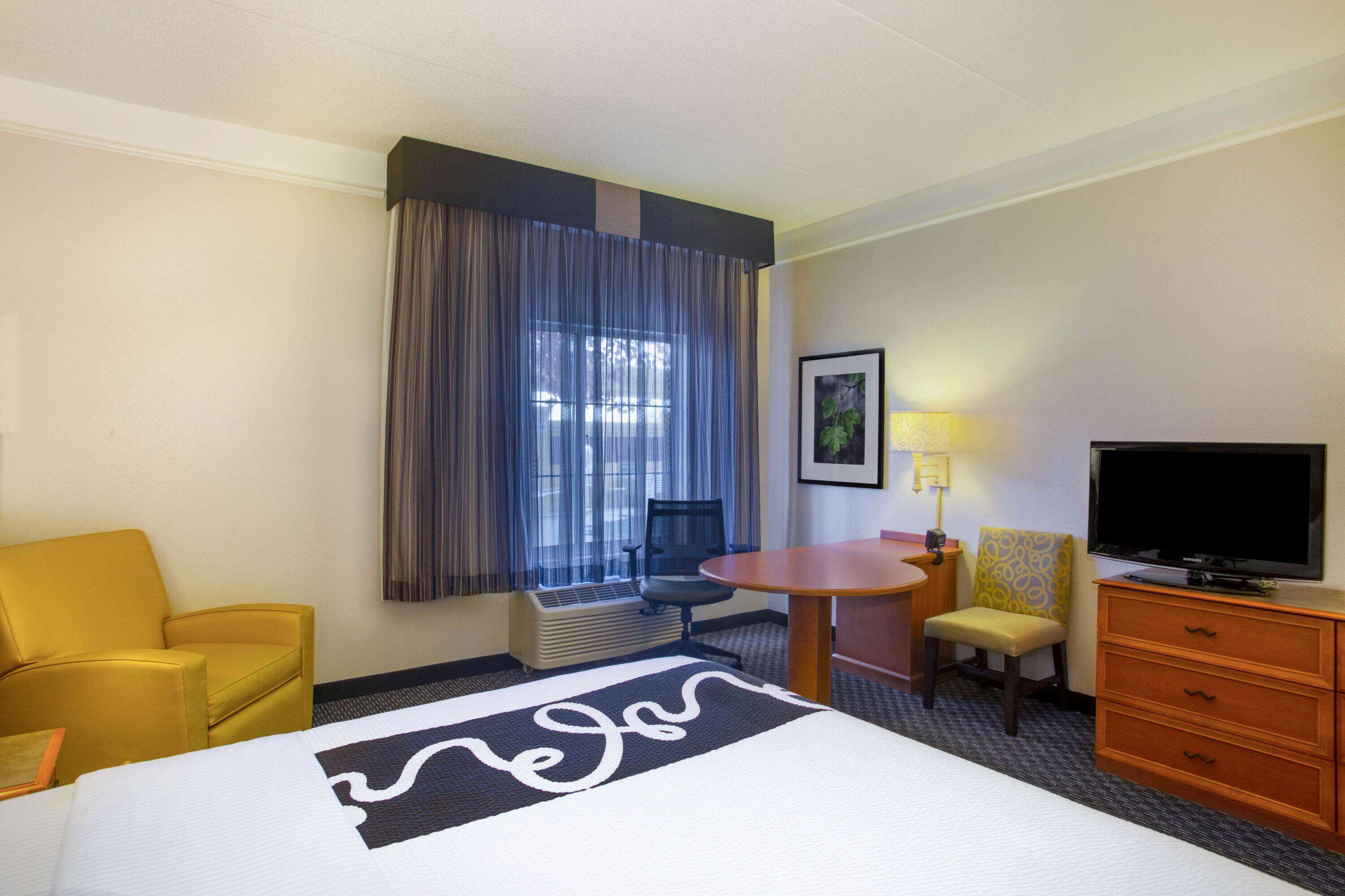 A hotel room with a large bed, a desk, a chair, a television, and a window with curtains.