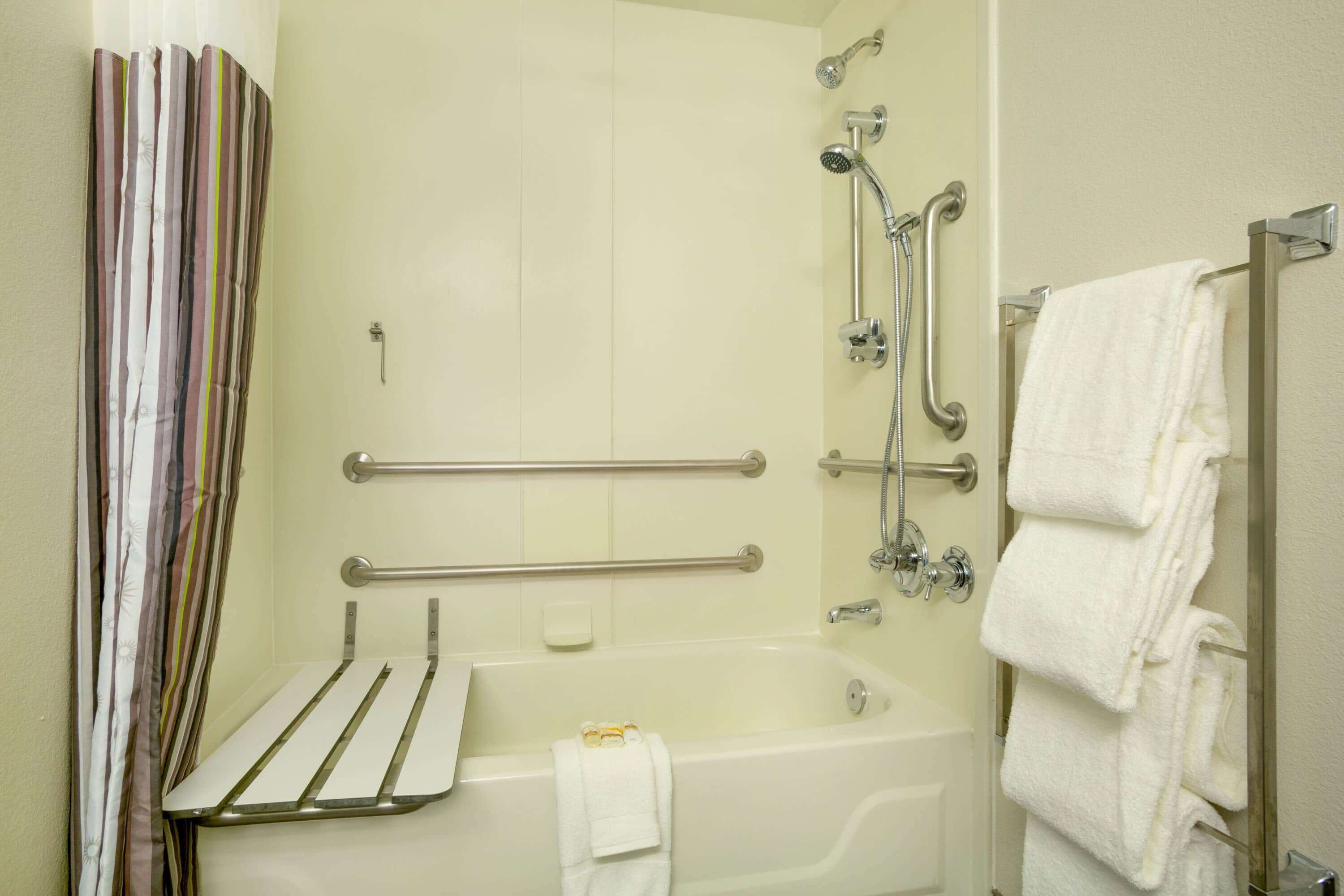 A bathroom with a shower, grab bars, a towel rack, and a toilet with a towel.