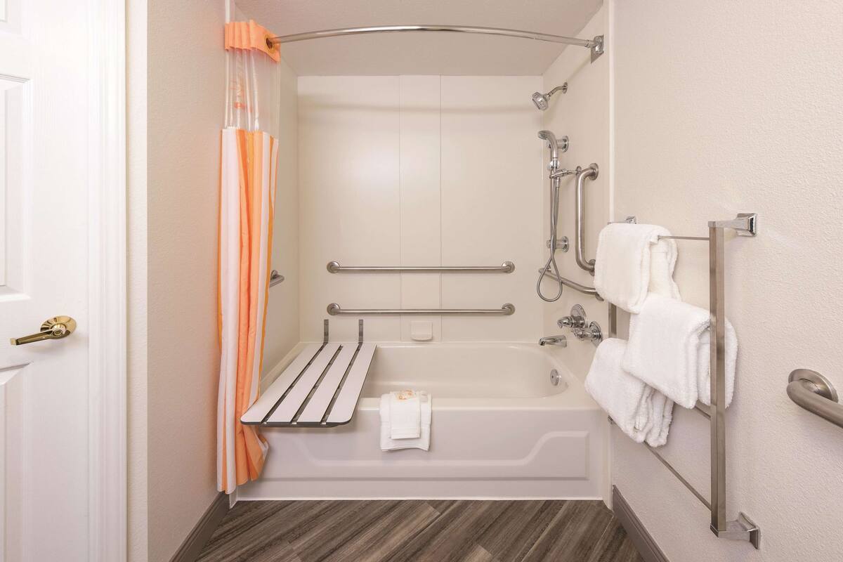 Une salle de bain équipée d’une baignoire, d’une douche, de barres d’appui, d’un porte-serviettes et d’une porte.