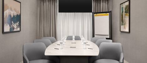 A conference room with a large table, six chairs, a flat-screen TV, and two framed pictures on the walls.
