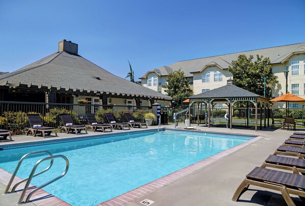A swimming pool with lounge chairs, a gazebo, and a covered area.