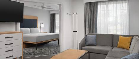 A hotel room with a bed, a sofa, a TV, a desk, and a ceiling fan.