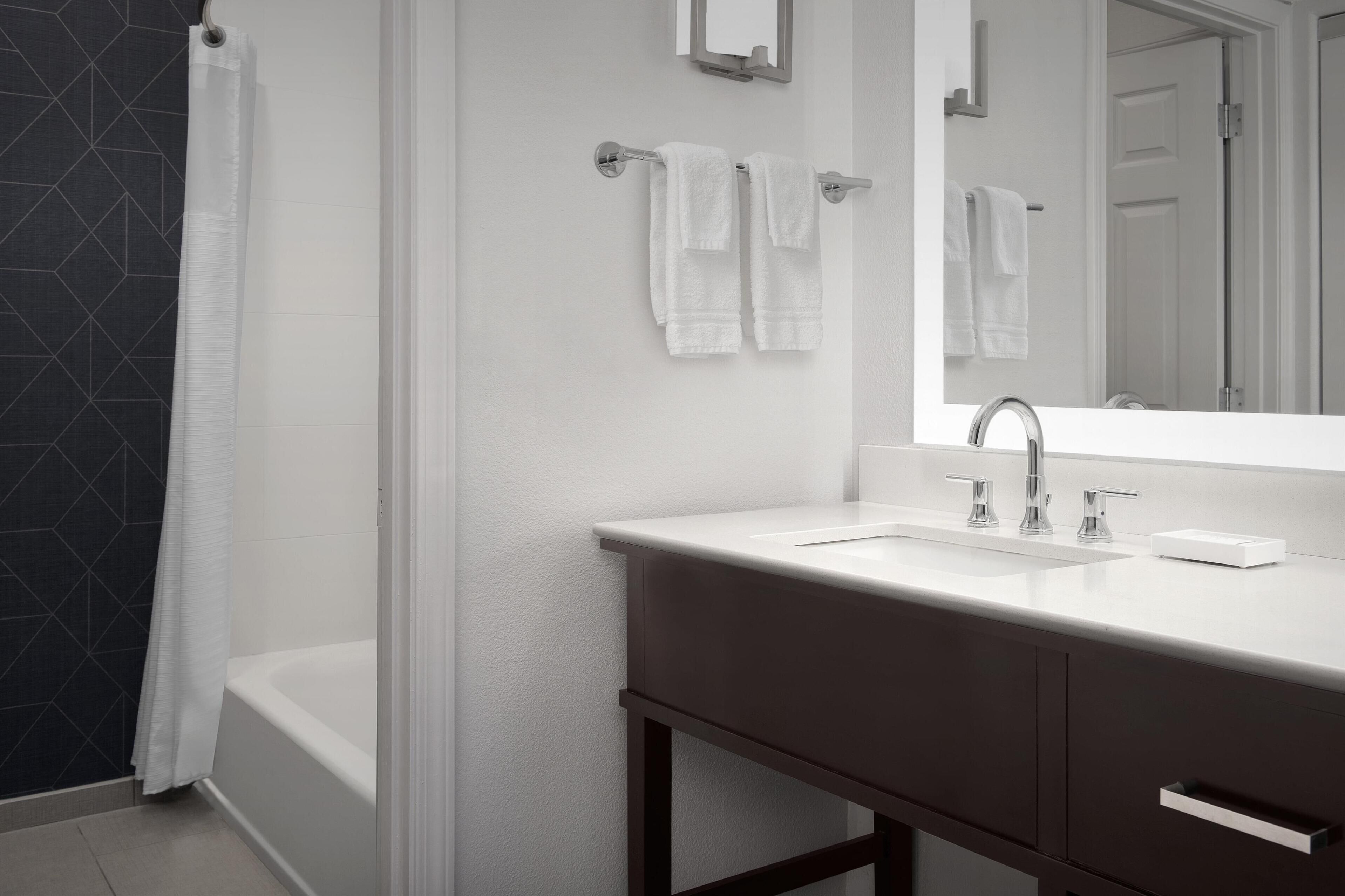 A modern bathroom with a bathtub, a large mirror, a white sink, and a dark wooden vanity.