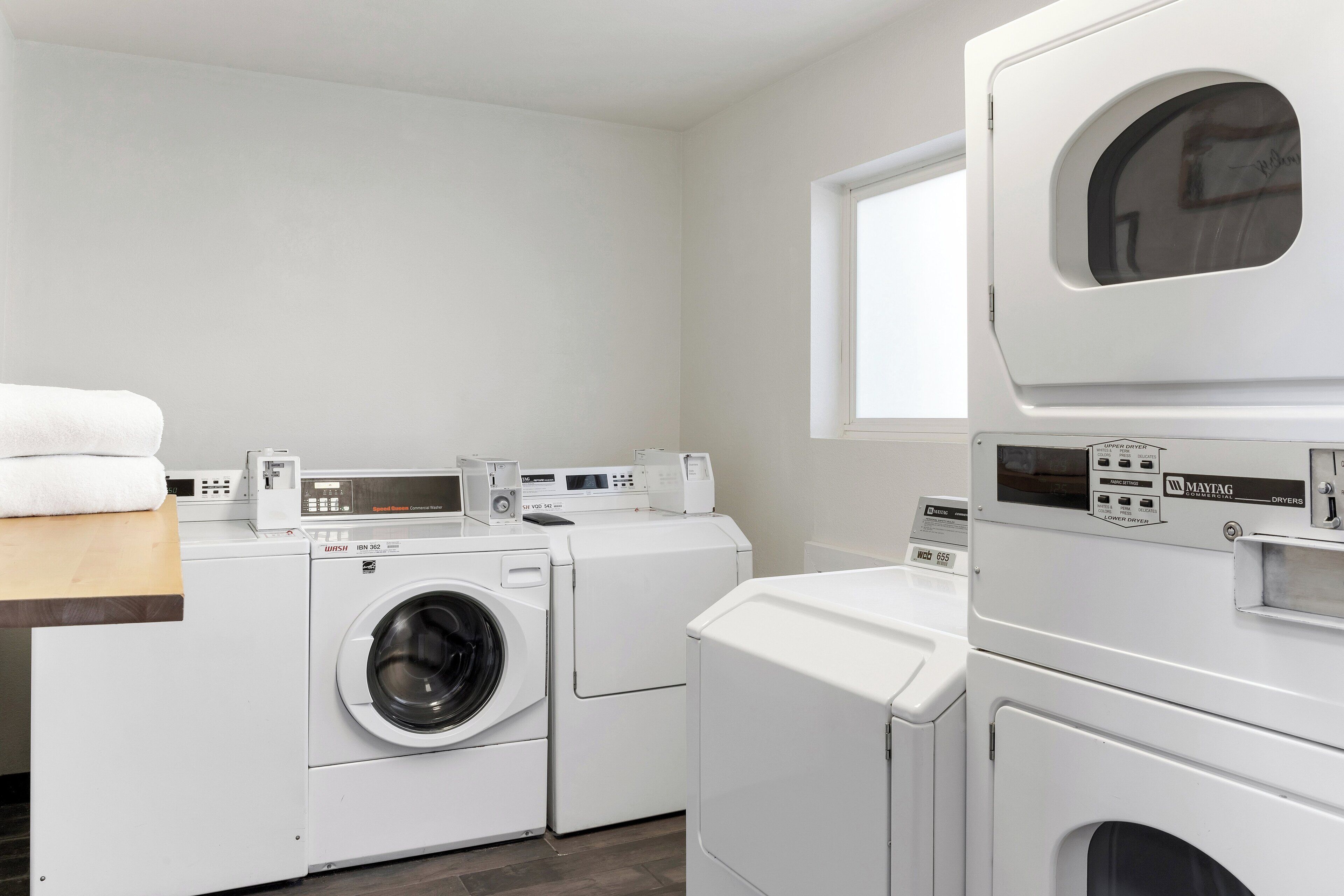 A modern laundry room with a front-loading washer and dryer, a control panel, and a window above the dryer.