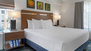 Une chambre d’hôtel avec un grand lit, deux tables de chevet avec des lampes, une tête de lit en bois et trois tableaux encadrés accrochés au mur.