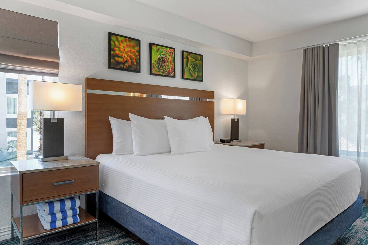 A hotel room with a large bed, two bedside tables with lamps, a wooden headboard, and three framed pictures on the wall.