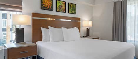 A hotel room with a large bed, two bedside tables with lamps, a wooden headboard, and three framed pictures on the wall.