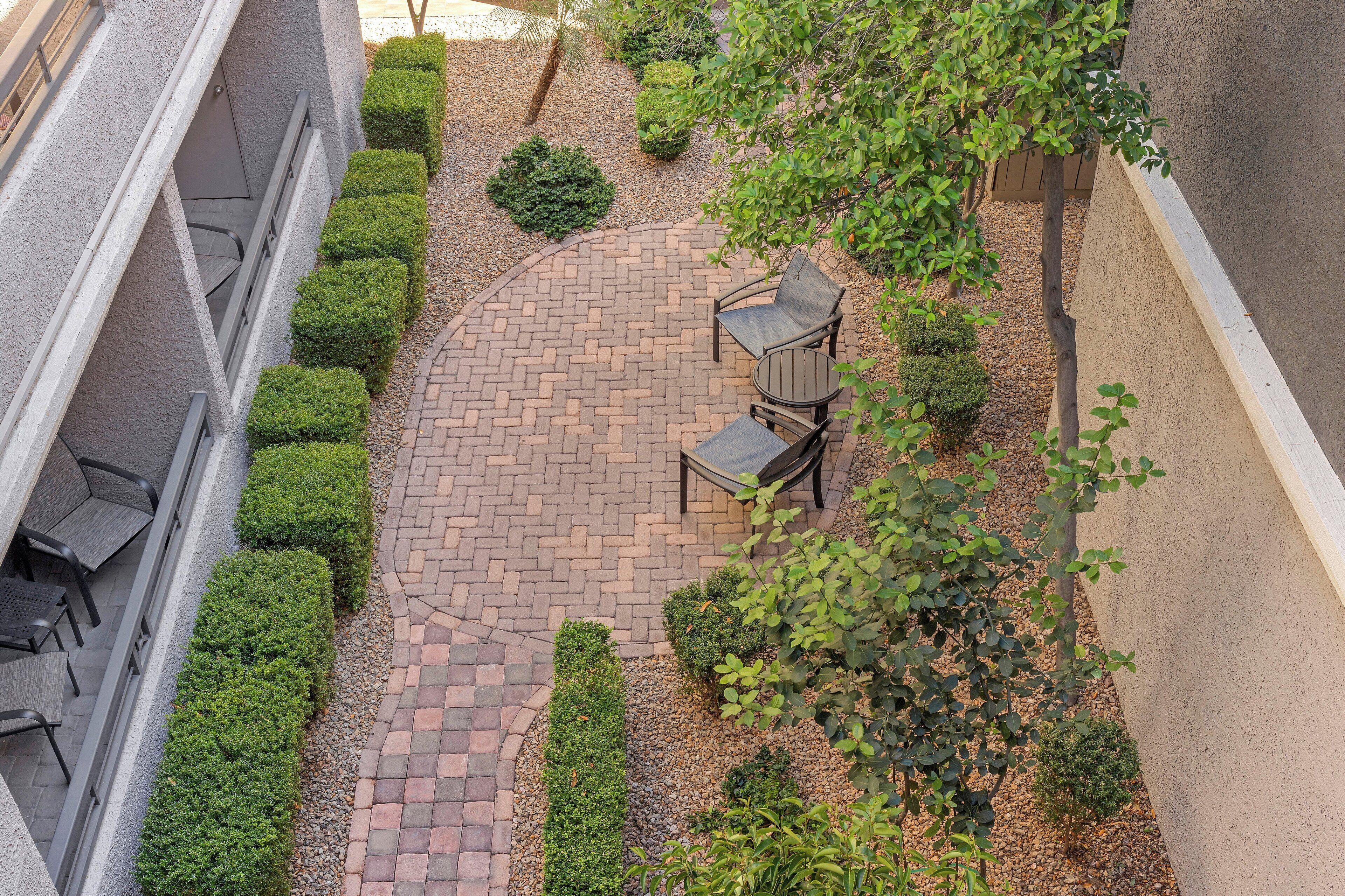 A courtyard with a brick patio, seating area, and trimmed bushes.