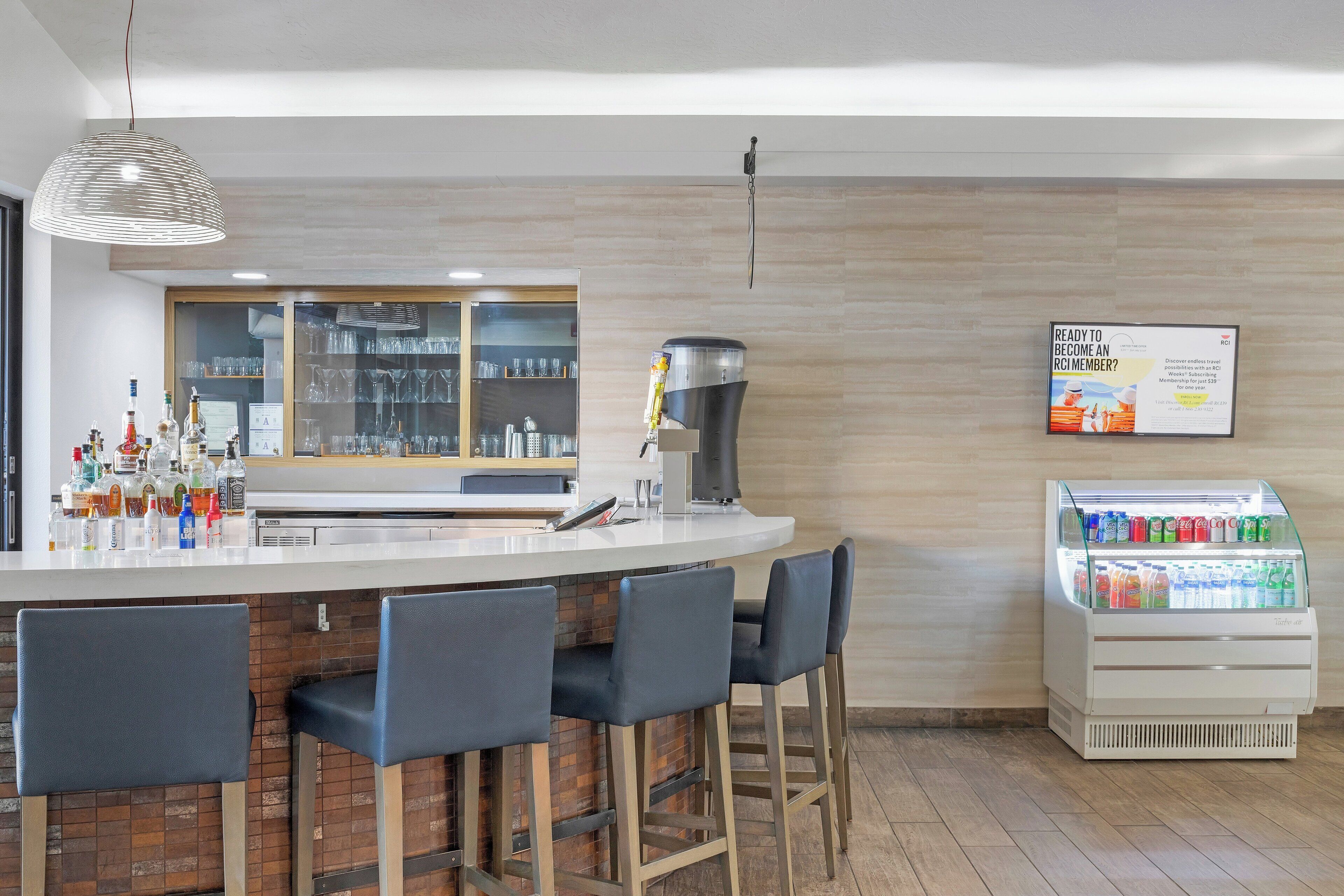 Zona de bar con mostrador, taburetes, dispensador de bebidas y vitrina refrigerada.