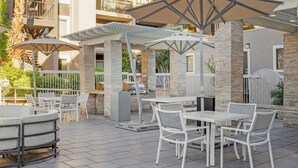 An outdoor patio with white furniture, umbrellas, and a barbecue grill. - Desert Rose Resort - No Resort Fee (Las Vegas)