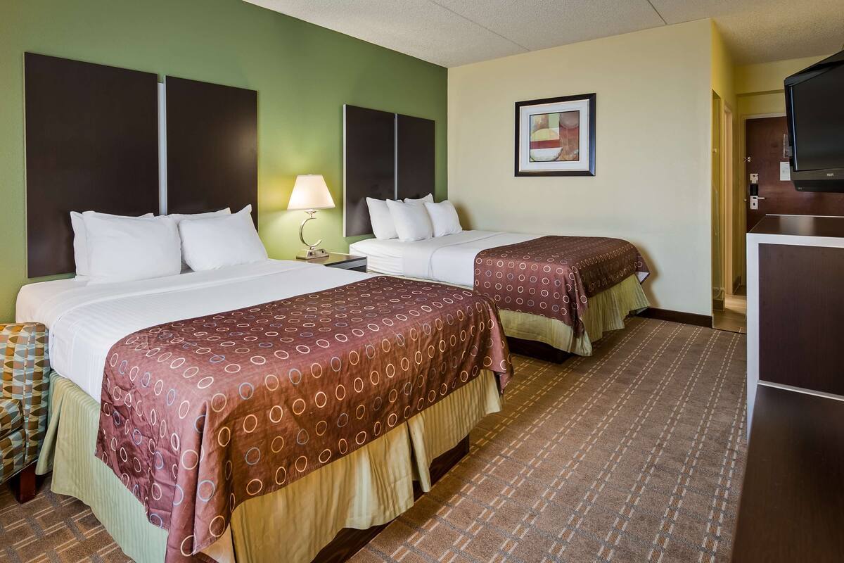 A hotel room with two beds, a sofa, a TV, and a framed picture on the wall.