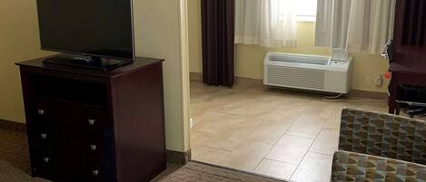 Habitación de hotel con cama, televisor en una cómoda, aire acondicionado y vistas al exterior a través de cortinas.