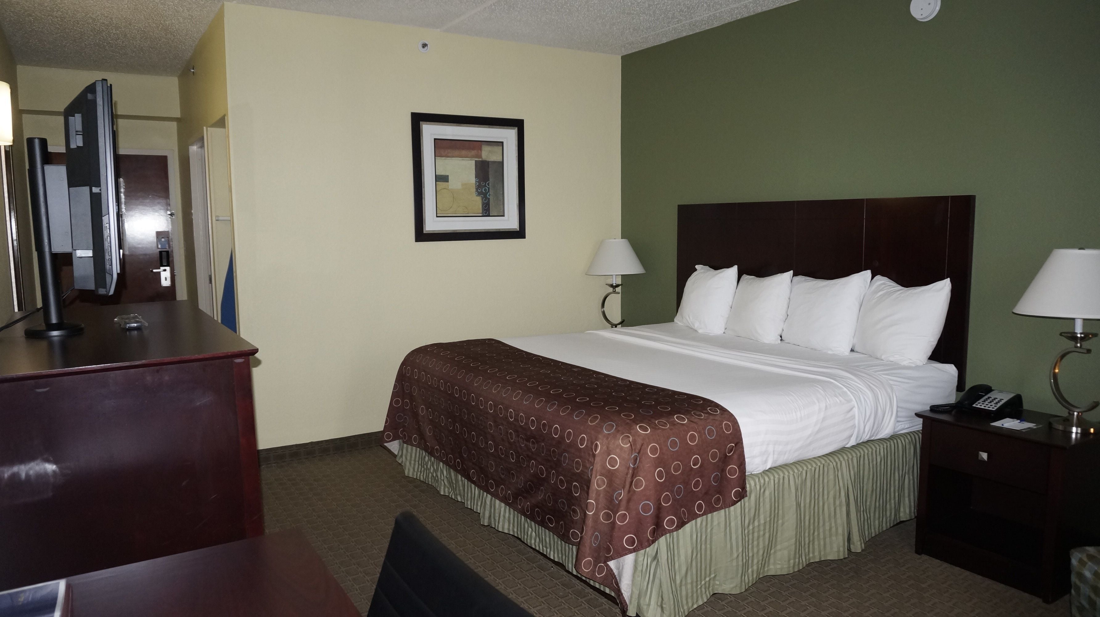 A hotel room with a large bed, two bedside lamps, a desk with a telephone, and a framed picture on the wall.
