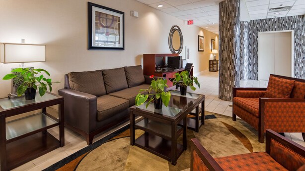 A hotel lobby with a brown sofa, a coffee table, and two armchairs. There are potted plants on the coffee table and a TV in the background. - Best Western Airport Inn & Suites Cleveland (Brook Park)