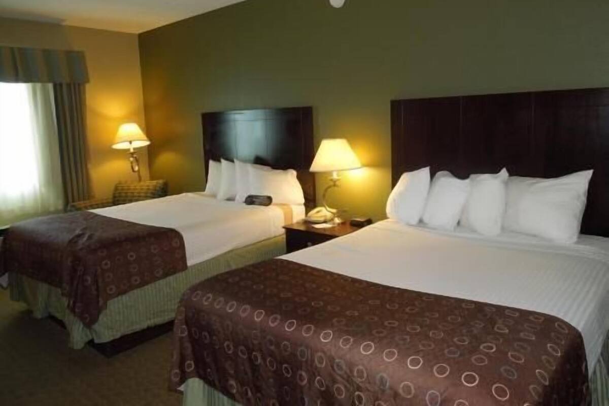 A hotel room with two beds, each with a headboard, bedside tables with lamps, and a window with curtains.