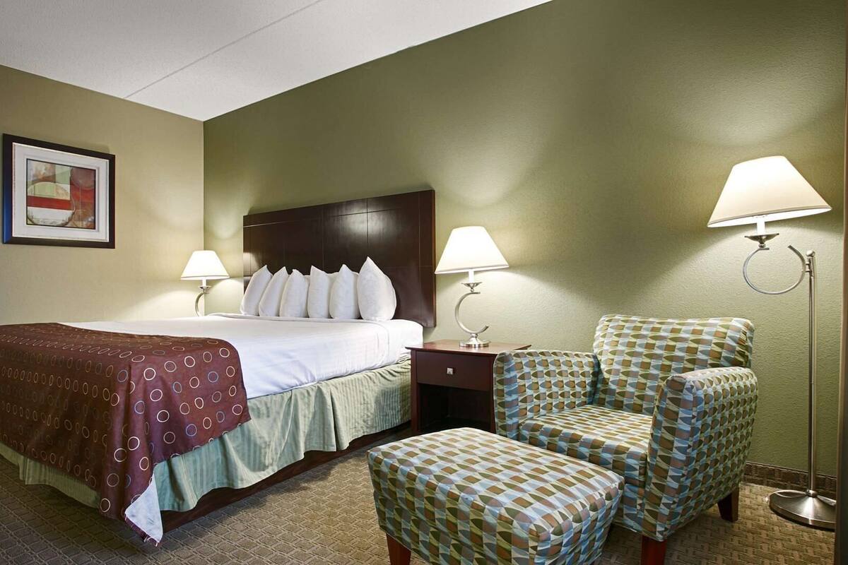 A hotel room with a bed, two bedside lamps, a chair, and a small table.