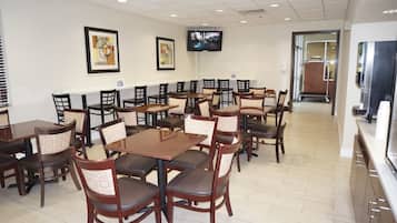Un restaurante con varias mesas y sillas, un televisor en la pared y una barra con una máquina de café.