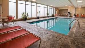 An indoor swimming pool with clear blue water, surrounded by red lounge chairs and potted plants. - Best Western Airport Inn & Suites Cleveland (Brook Park)