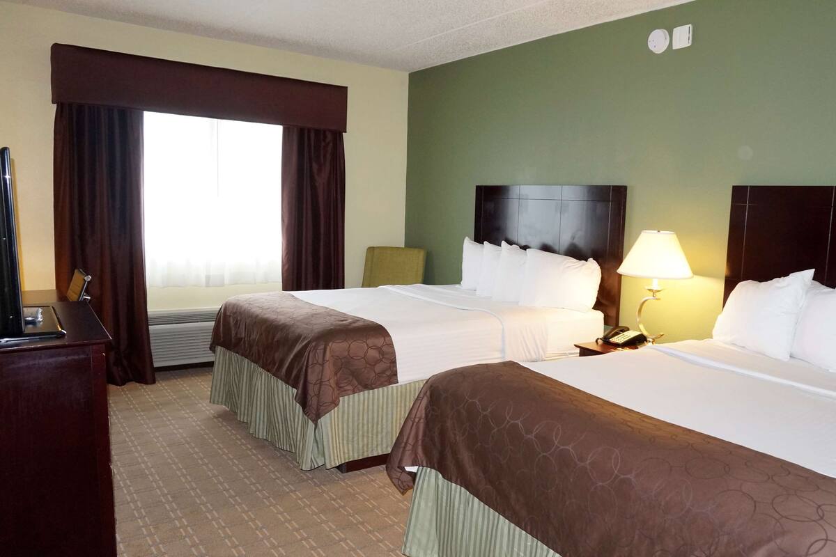 A hotel room with two beds, a desk, a telephone, and a lamp.
