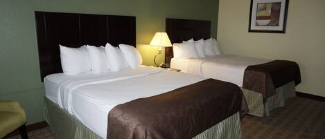 A hotel room with two beds, a nightstand with a lamp, a framed picture on the wall, and a chair.