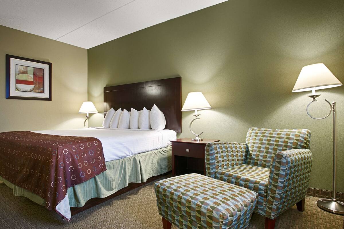 A hotel room with a bed, two bedside lamps, a chair, and a floor lamp.